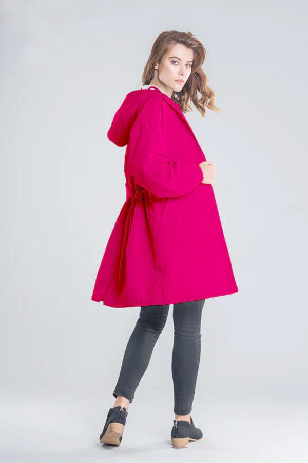 Woman wearing vibrant Barbara Pink Raincoat windbreaker jacket with hood, side view on gray background