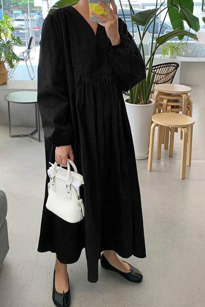 Woman wearing a black midi long sleeve spring dress holding a white handbag in a modern indoor setting