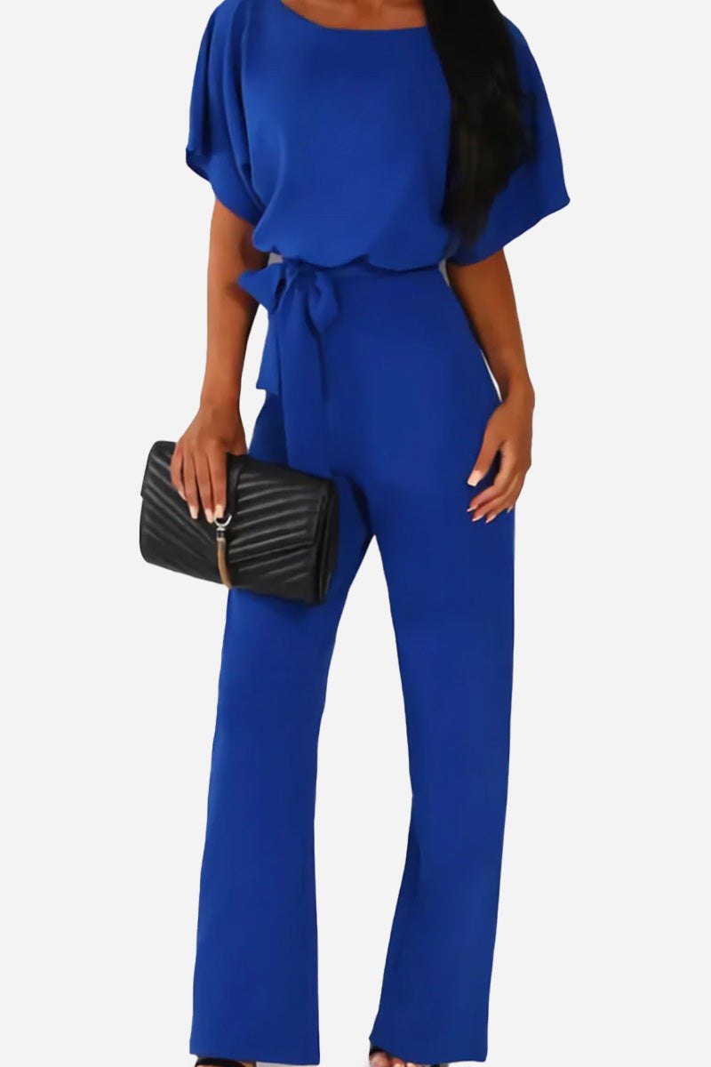 Woman wearing chic short-sleeved wide-leg blue jumpsuit with belt and black clutch bag
