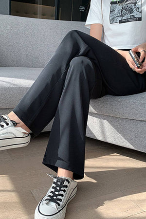 Casual loose wide-leg high-waisted black pants worn with white sneakers sitting on a couch
