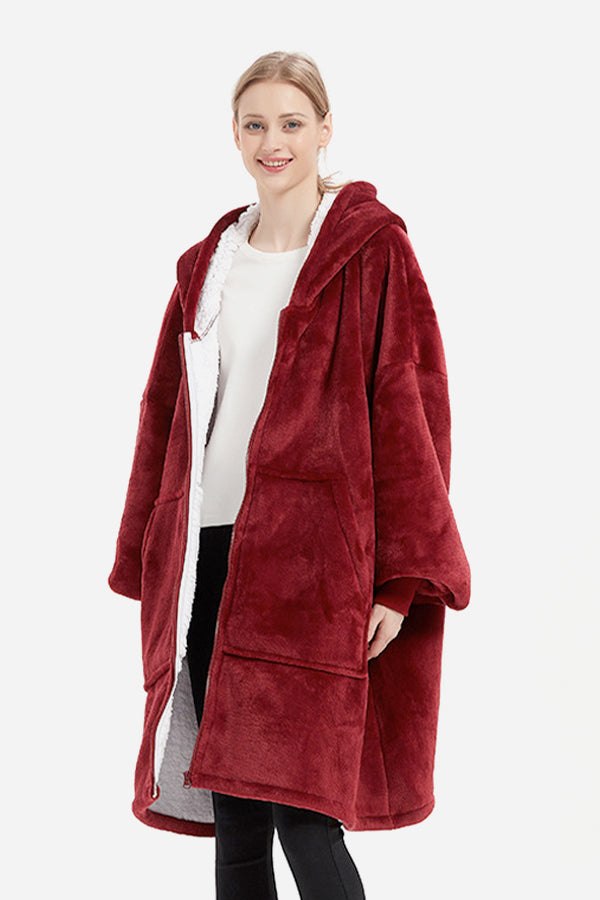 Woman wearing oversized ultra soft hooded blanket in deep red with front pockets and zipper closure
