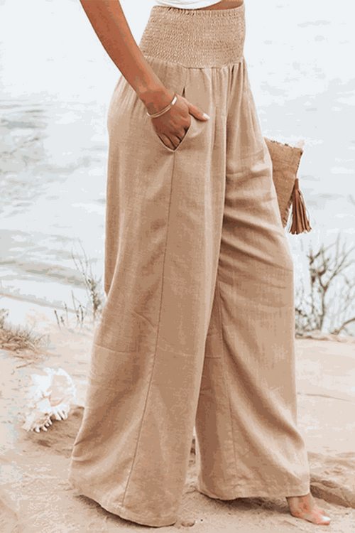 Woman wearing beige high-waist cotton linen palazzo pants with wide legs and pockets on beach