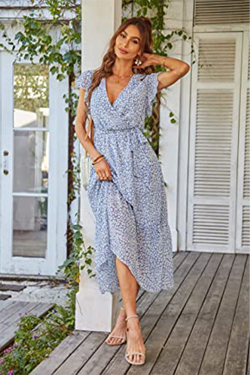 Woman wearing Elegant Blossoms Boho Maxi Dress with floral pattern, V-neck, ruffled sleeves, and belted waist standing on porch.