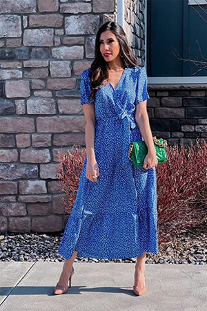 Woman wearing a blue charming floral boho maxi dress with short sleeves and a wrap V-neck standing outdoors near a stone wall.