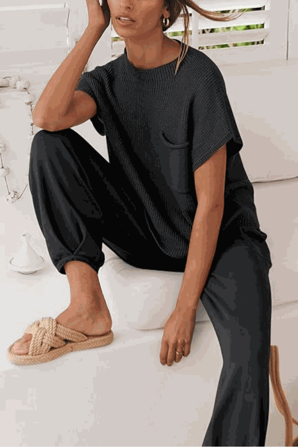 Woman wearing black Comfy Couture Knit Sweater two-piece set with short sleeve top and high-waisted pants sitting indoors