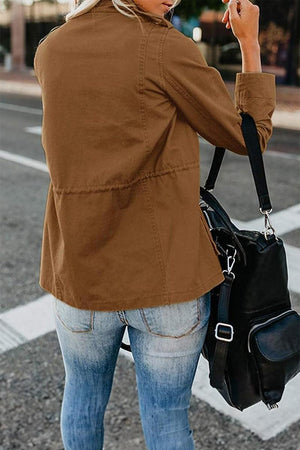 Woman wearing brown fashion cargo utility jacket with adjustable waist and multiple pockets, styled casually with jeans and black bag outdoors