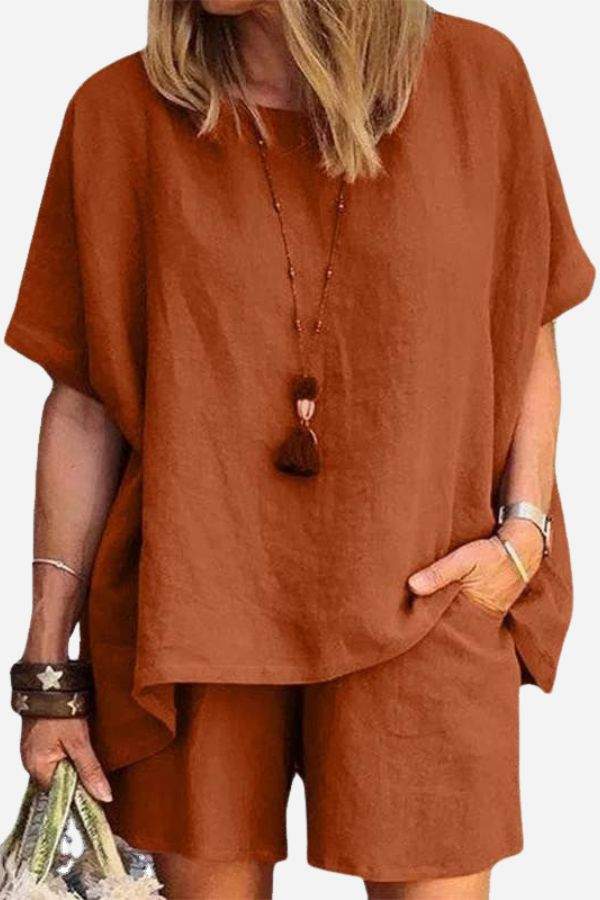 Woman wearing comfy linen-like rust-colored shirt and shorts two-piece set with relaxed fit and short sleeves, accessorized with bracelets and necklace.