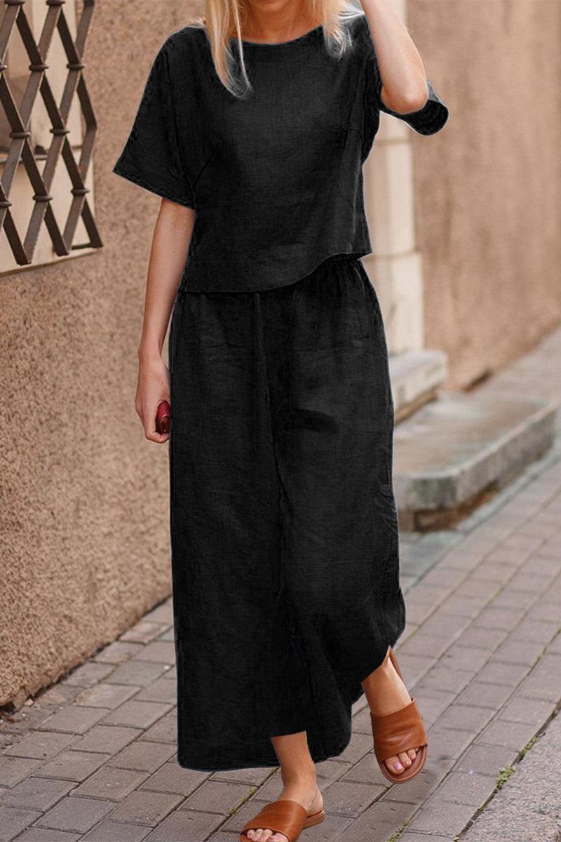 Woman wearing black loose fit co-ord set with short sleeves and wide-leg pants walking on cobblestone street