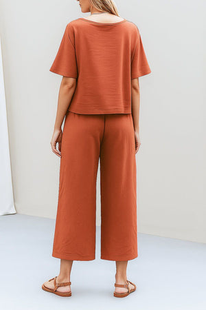 Back view of a woman wearing rust-colored loose fit co-ord set with a soft-tailored short sleeve top and wide-leg pants paired with sandals.