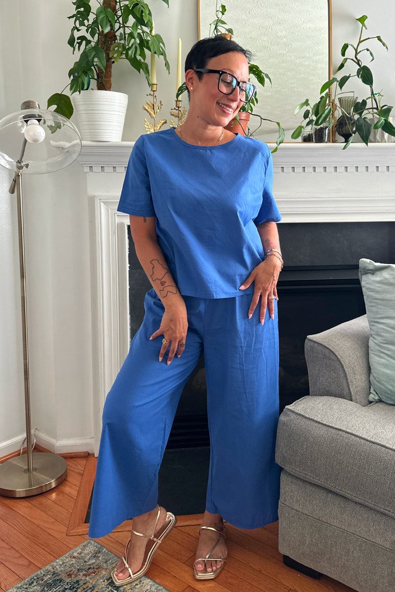Woman wearing blue loose fit co-ord set with short sleeves and wide-leg trousers in a cozy living room setting