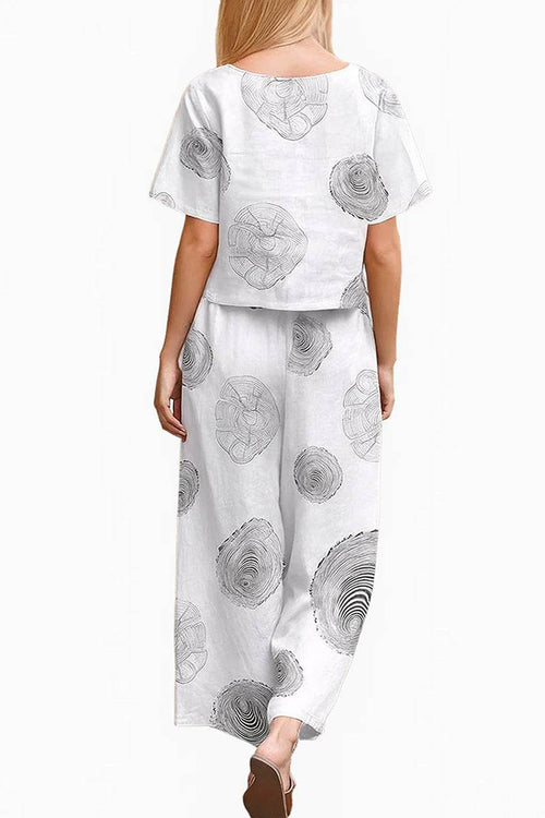 Woman wearing white loose fit co-ord set with black floral prints and wide-leg pants from back view