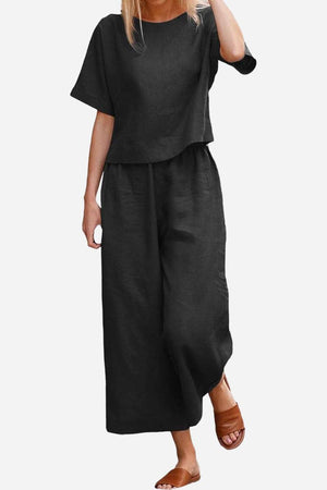 Woman wearing a black loose fit co-ord set with wide-leg trousers and a relaxed short sleeve top paired with brown sandals