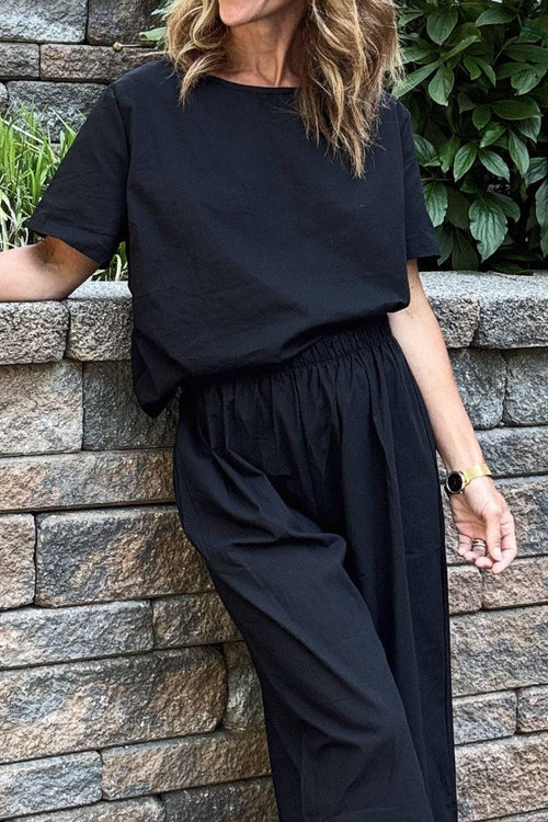 Woman wearing black loose fit co-ord set with short-sleeve top and wide-leg elastic waist trousers outdoors against stone wall