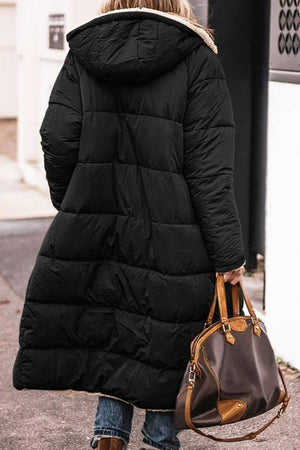 Black Sherpa-lined hooded teddy coat with a long puffer design and large pockets worn by a woman carrying a brown handbag outdoors