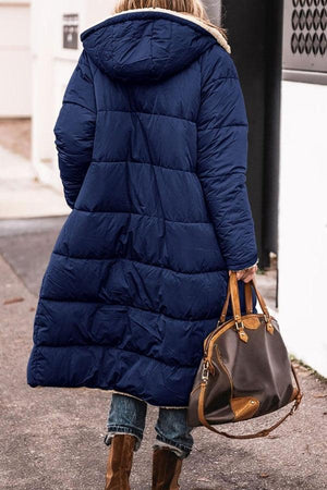 Woman wearing navy Sherpa-lined hooded teddy coat with quilted puffer design and carrying brown handbag outdoors