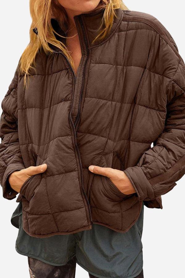 Woman wearing a brown lightweight puffer travel jacket with hands in pockets and zippered front