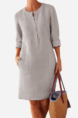 Lightweight gray cotton dress with rolled 3/4 sleeves, front buttons, and pockets, styled with a casual brown woven handbag.