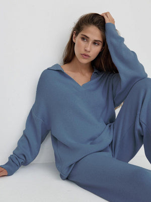 Woman wearing plush preppy blue two-piece loungewear set with polo collar and wide leg pants sitting against white wall