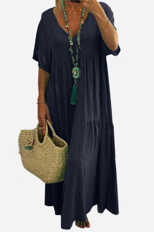 Woman wearing navy blue V-neck two-tiered maxi swing dress with short sleeves and carrying a woven straw bag.