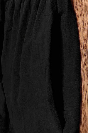 Black capped-sleeve voluminous pleated midi dress with airy sleeves and pockets on wood floor background