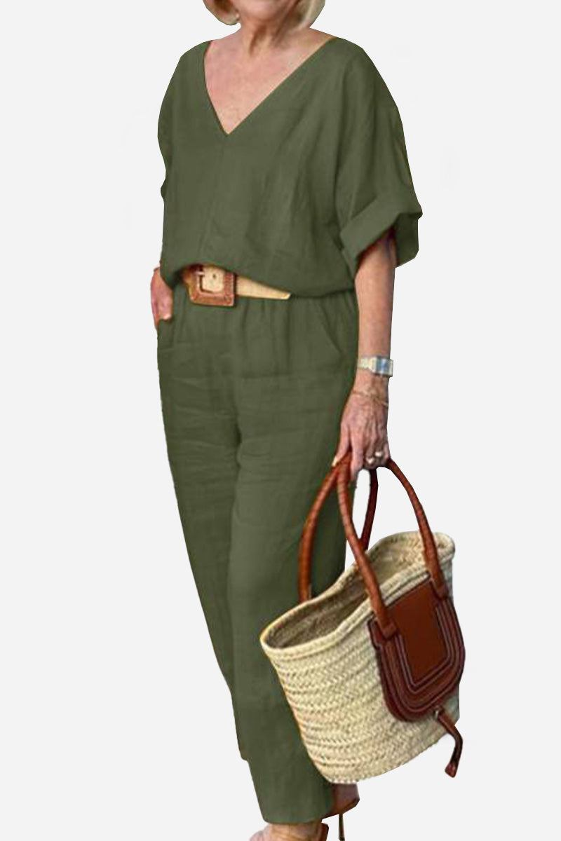 Woman wearing olive green V-neck cotton two-piece trouser set with rolled sleeves and belted waist holding woven handbag