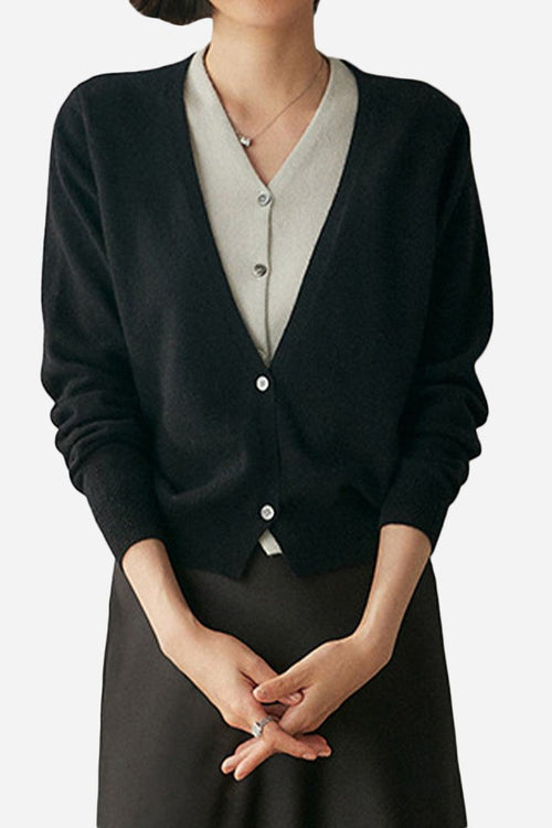 Woman wearing black single-breasted cashmere wool cardigan with V-neck and buttons over light gray top.