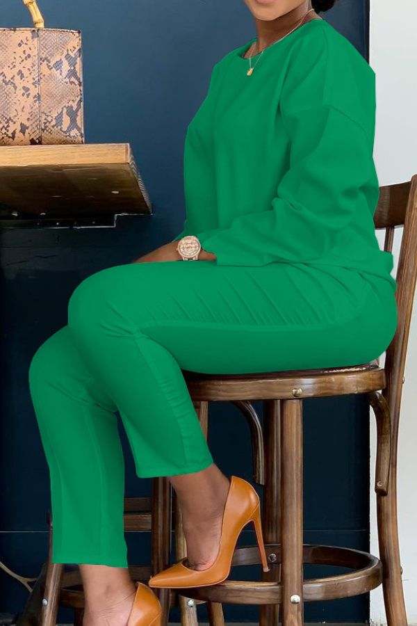 Woman wearing vibrant green cotton two-piece set sitting on wooden chair with tan high heels and snake-print handbag nearby