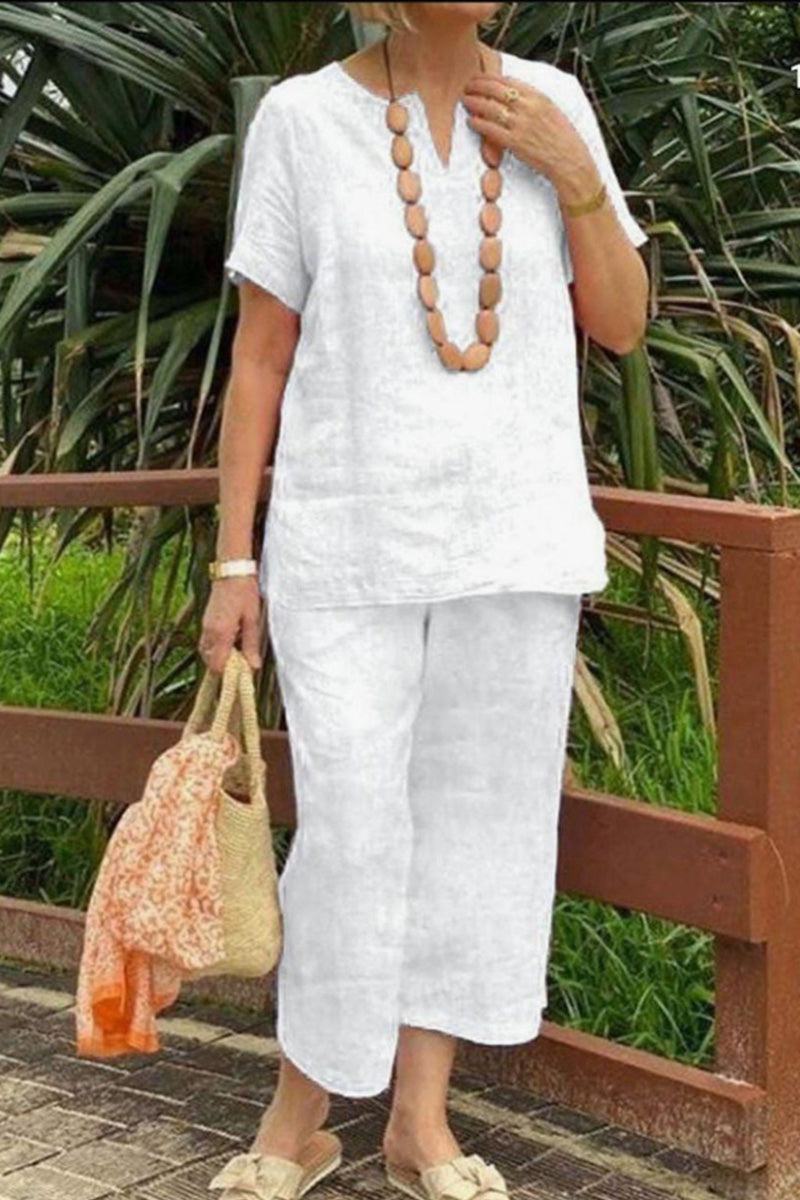 Woman wearing white Breezy Cotton Blend relaxed fit two-piece set with short sleeves and elastic waist pants, accessorized with wooden bead necklace and straw bag.