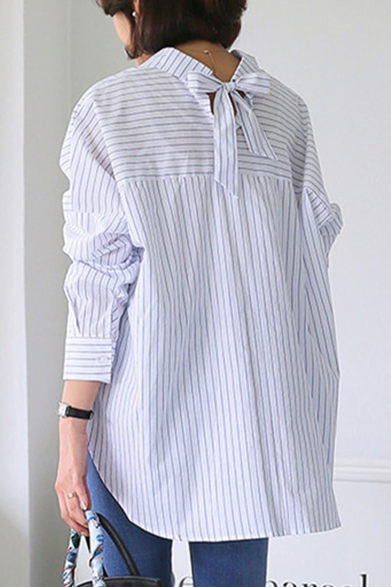 Back view of a woman wearing a 100% cotton oversized striped shirt with a bow detail at the neck and long sleeves.
