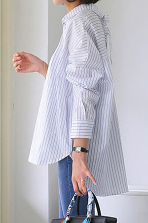 Side view of a person wearing a 100 cotton oversized striped shirt with rolled sleeves and blue jeans, holding a patterned handbag