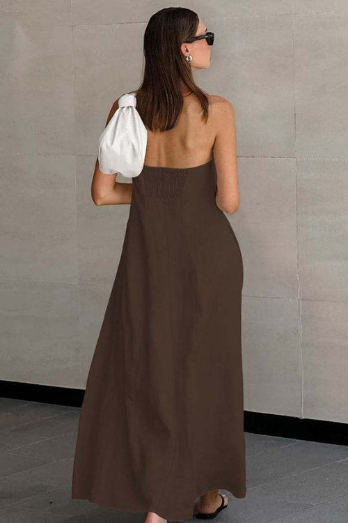 Woman wearing brown strapless long dress made from breathable cotton linen blend fabric, carrying white handbag, standing against gray tiled wall