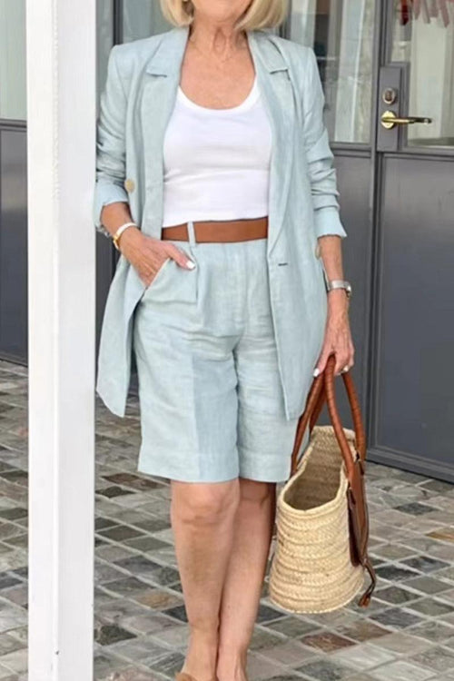 Stylish blazer and shorts two-piece set in light pastel, worn with white tank top and brown belt, paired with woven handbag.