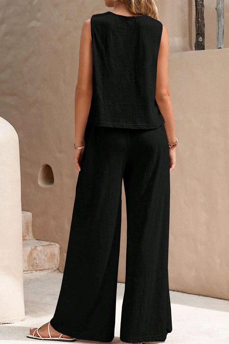 Woman wearing black sleeveless wide leg pants set standing against beige textured wall