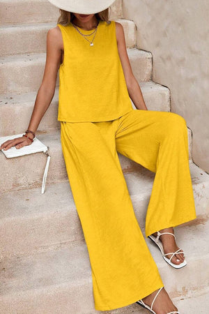 Woman wearing a mustard yellow sleeveless wide leg pants set with white sandals and a white clutch bag sitting on stairs
