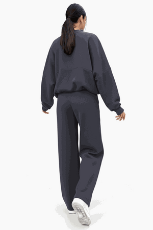 Woman wearing The Voyager Zip Set in dark charcoal, featuring a relaxed zip-front sweatshirt and wide-leg joggers with pockets, styled for comfort and travel.