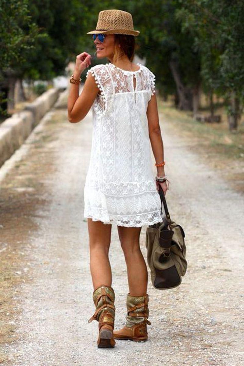 Woman wearing white pom pom lace mini dress with sleeveless design and carrying a bag on a path outdoors