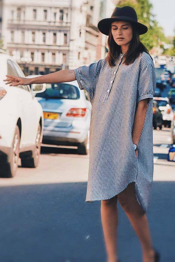 Woman wearing a striped linen blend gauze shirt dress with short sleeves and knee length, styled with a black hat on a city street