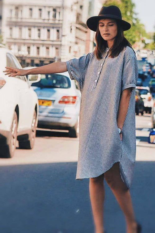 Woman wearing a striped linen blend gauze shirt dress with short sleeves and knee length, styled with a black hat on a city street