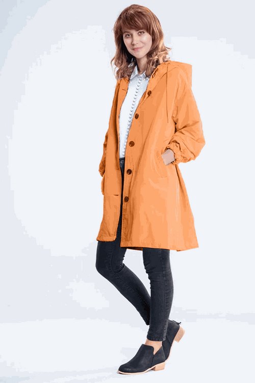 Woman wearing orange water-resistant oversized hooded windbreaker rain jacket with black pants and black shoes