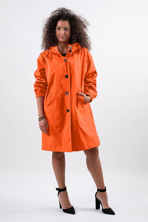 Woman wearing bright orange water-resistant oversized windbreaker rain jacket with hood and buttons