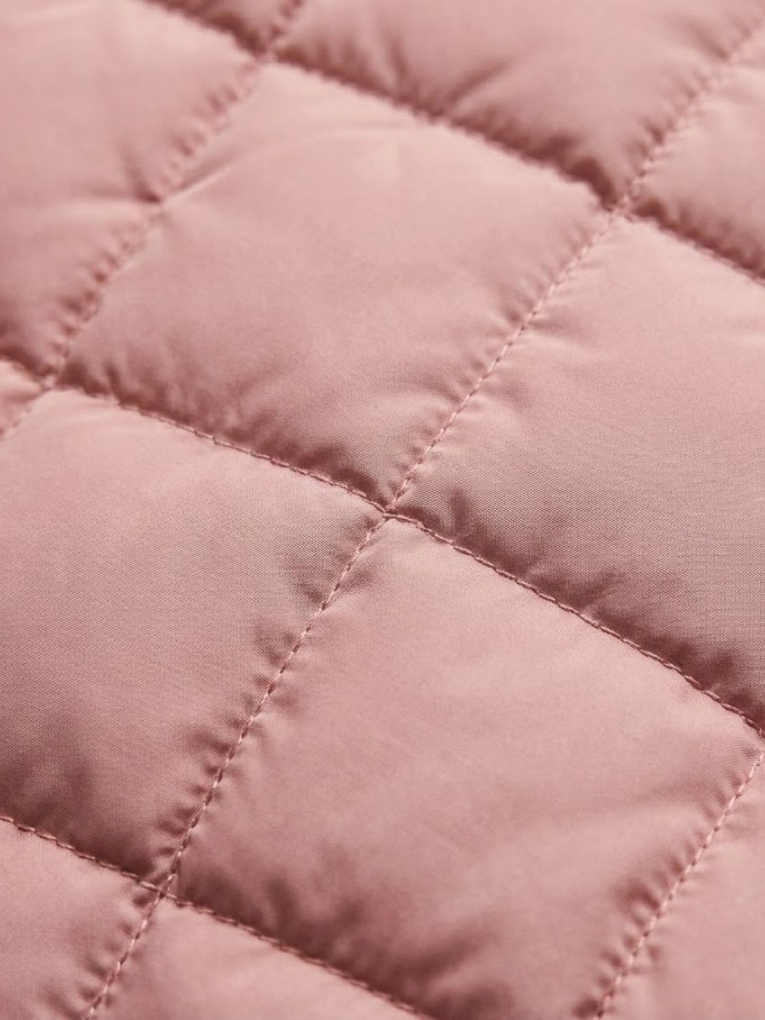 Close-up of pink quilted fabric on lightweight puffer travel jacket