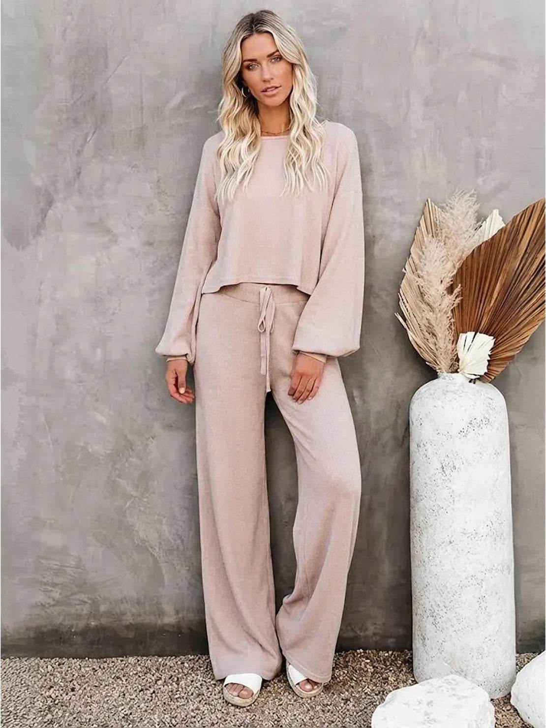 Woman wearing a beige round neck loose fit cozy two-piece set with wide-leg pants against gray textured wall