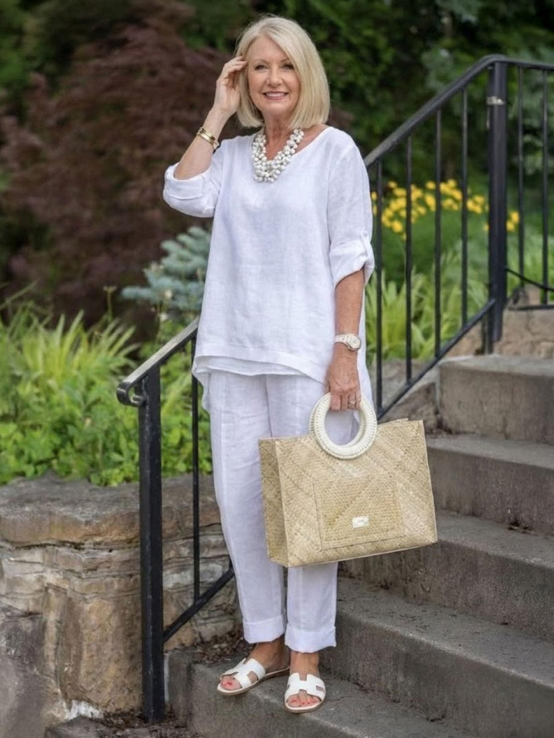 woman wearing white asymmetrical two-piece trouser set with rolled sleeves and tapered pants carrying woven handbag outdoors