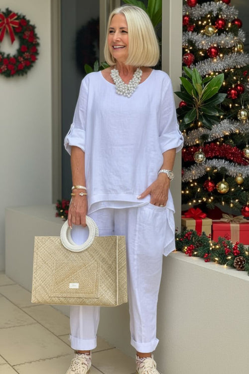 woman wearing white asymmetrical two-piece trouser set with rolled sleeves and holding a straw handbag near Christmas decorations