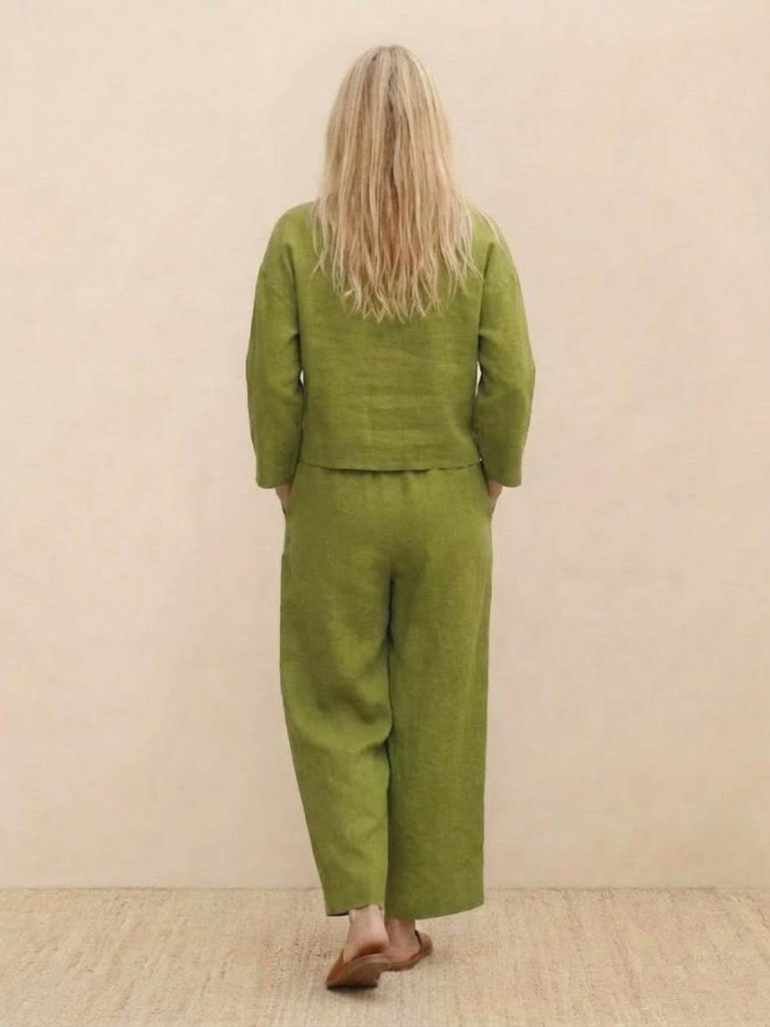 Woman wearing a green loose solid color two-piece set with long sleeves and wide-leg pants seen from the back
