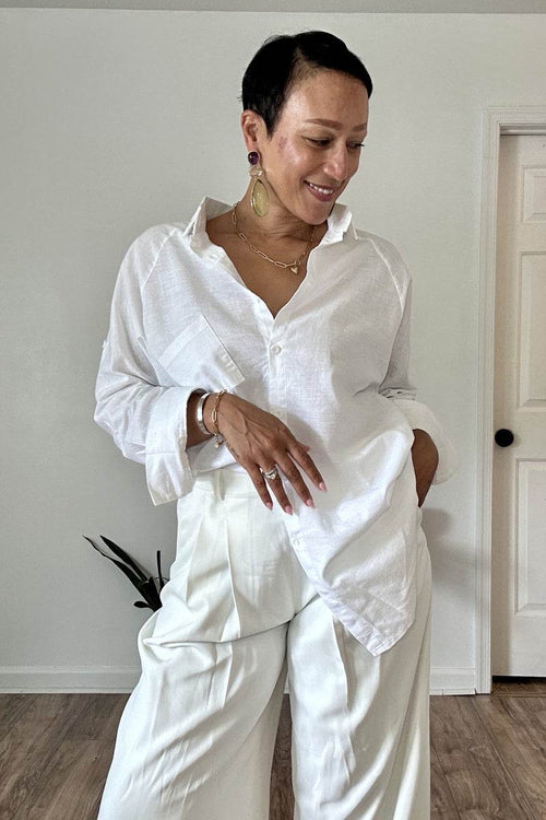 Woman wearing a white oversized linen shirt with relaxed fit and flowing hem paired with white pants indoors