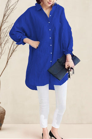 Woman wearing blue oversized linen shirt with white pants holding black clutch bag
