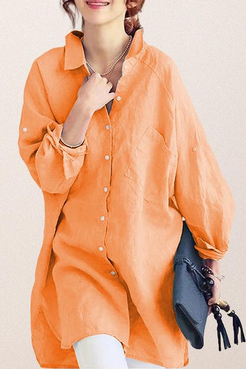 Woman wearing oversized orange linen shirt with rolled-up sleeves holding a gray clutch bag