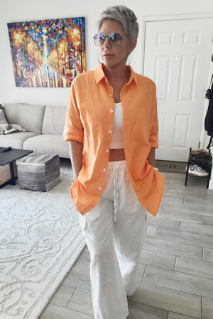 Woman wearing oversized orange linen shirt with white pants indoors