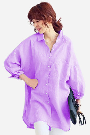 Woman wearing oversized linen shirt in lavender, loose fit with button front and balloon sleeves, styled casually with white pants and black clutch.
